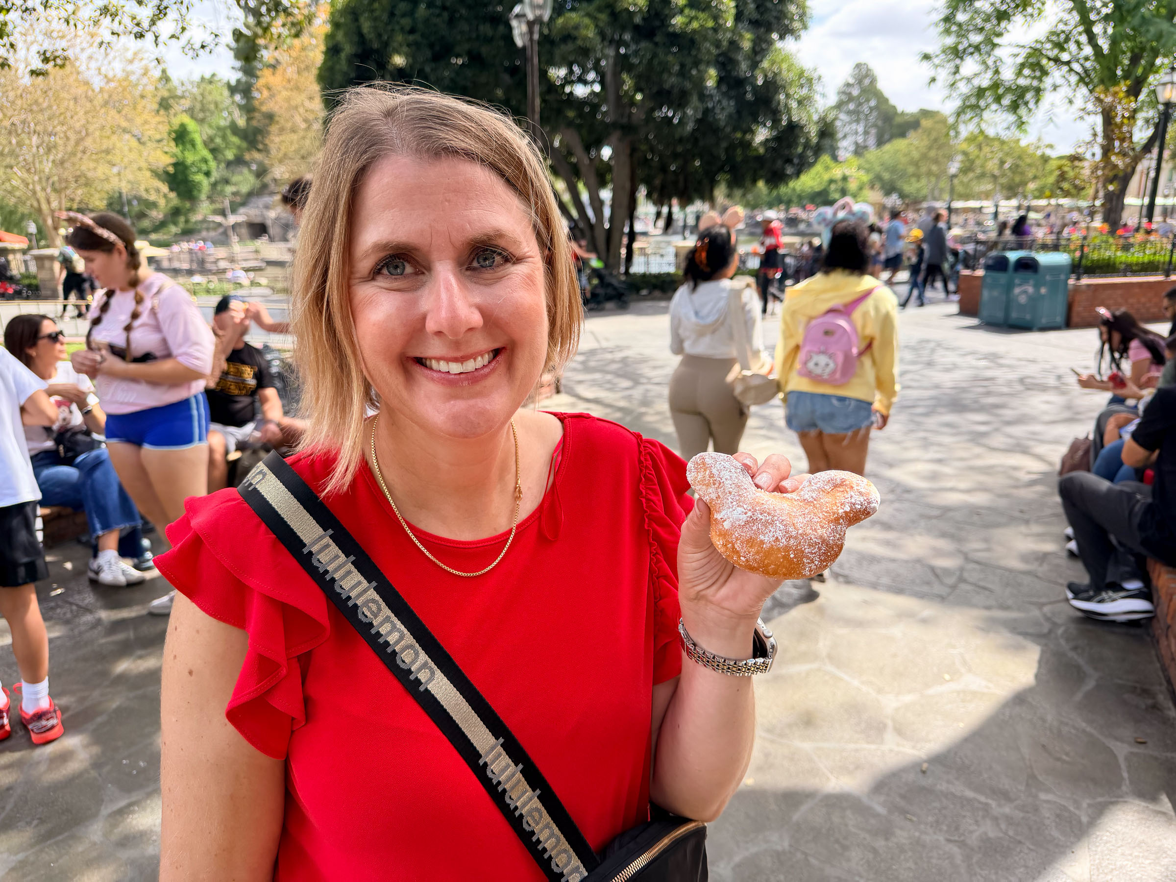 Smiling with a Mickey beignet in a Disney park plaza