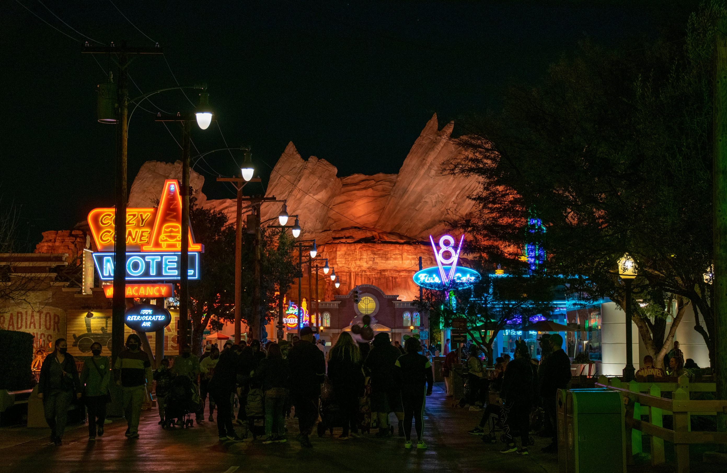 Cars Land at Disney California Adventure at dusk with neon signs glowing and Ornament Valley in the background.