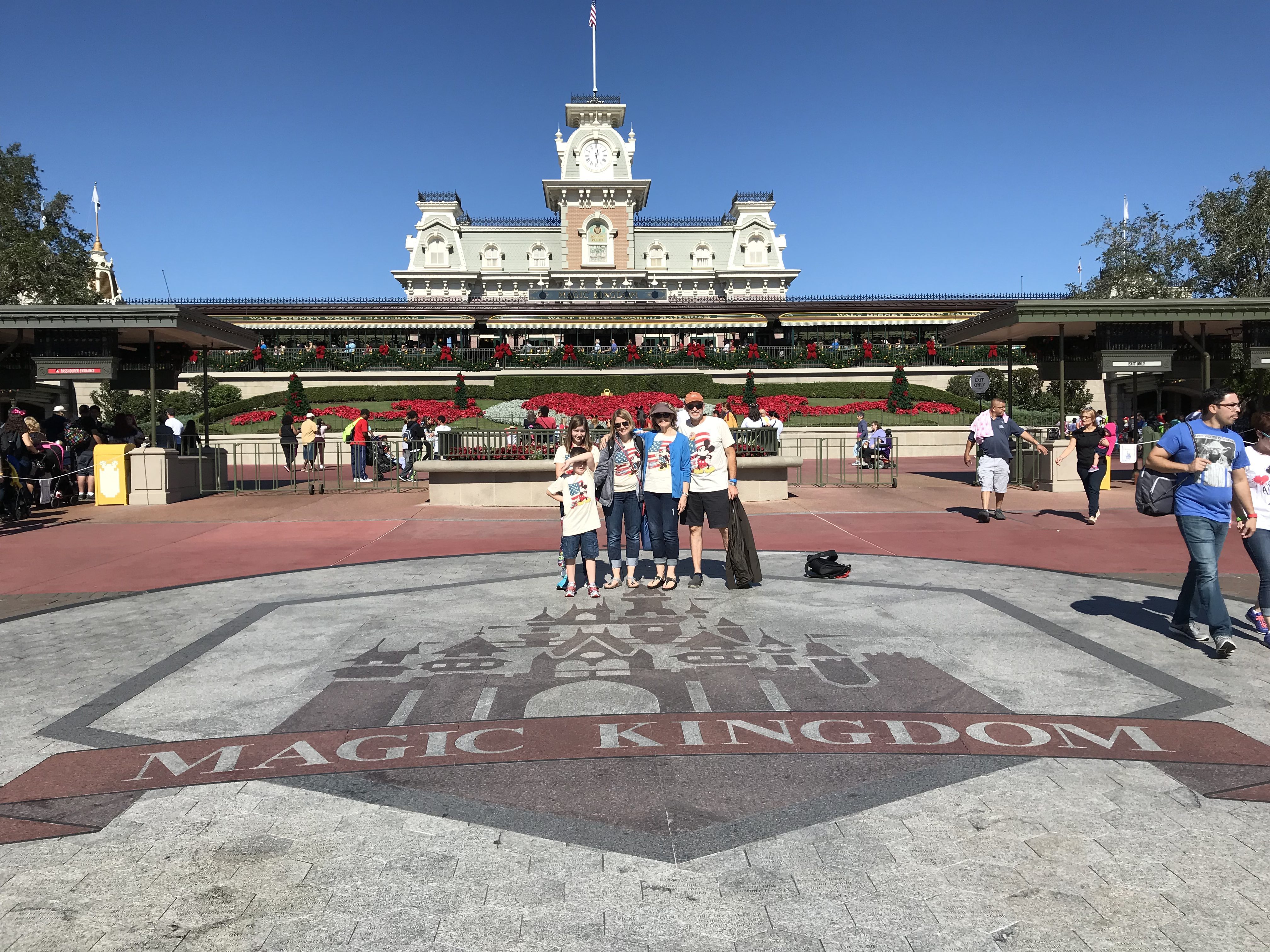 Family posing on the Magic Kingdom entrance medallion with the train station behind them at Walt Disney World.