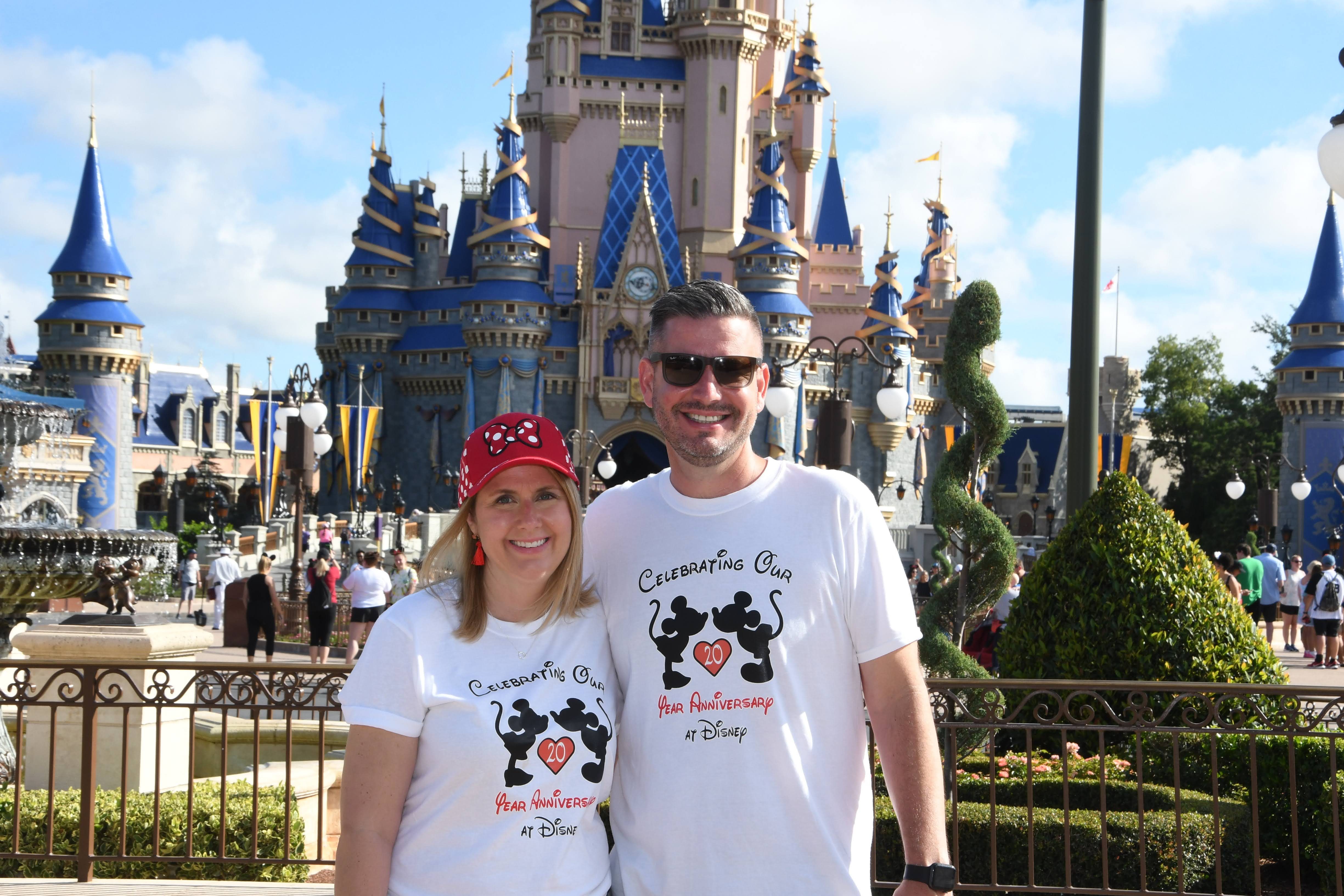 Couple in 20th anniversary Disney shirts posing in front of Cinderella Castle at Magic Kingdom.