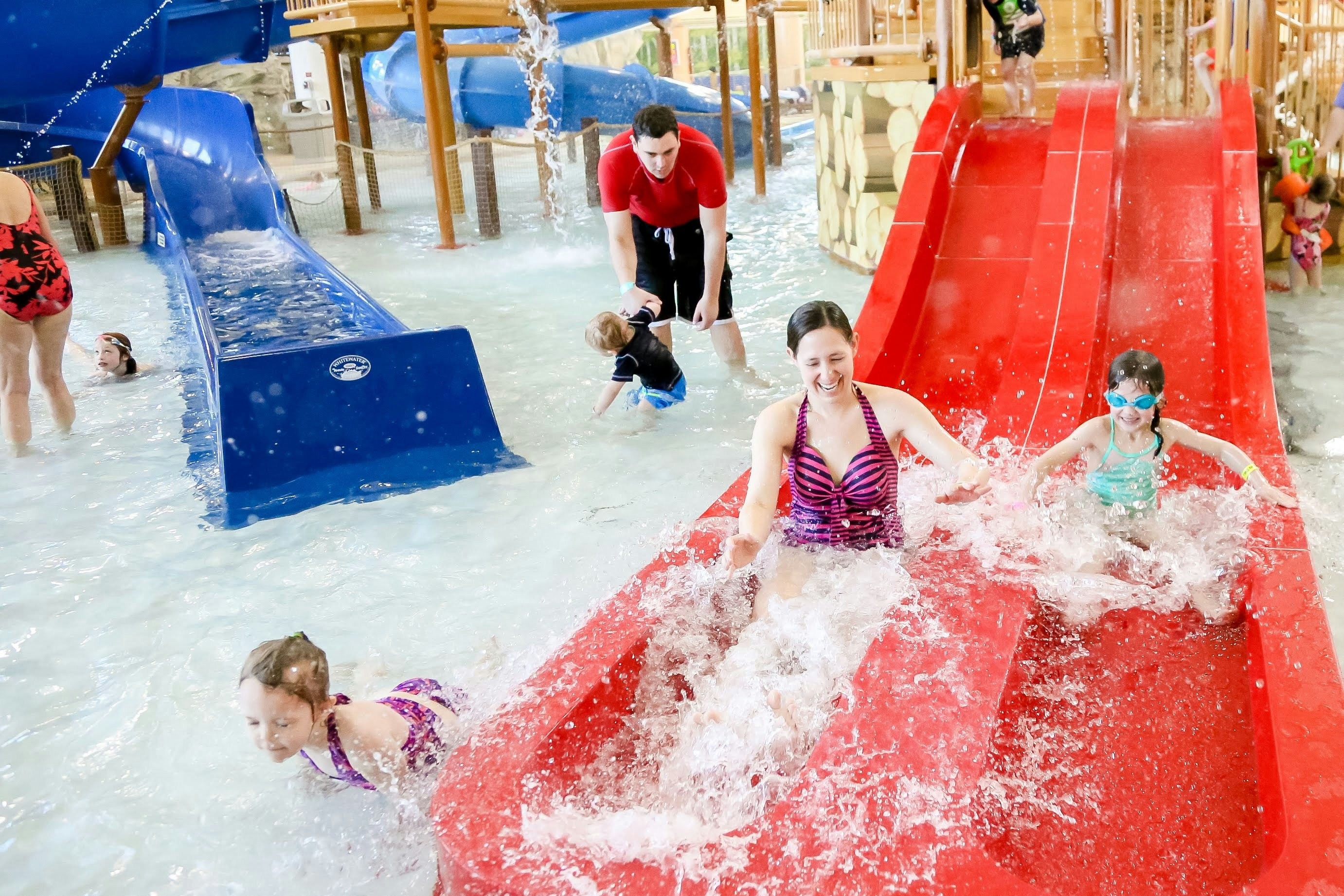 Family enjoying water slides and splashing down at an indoor water park.