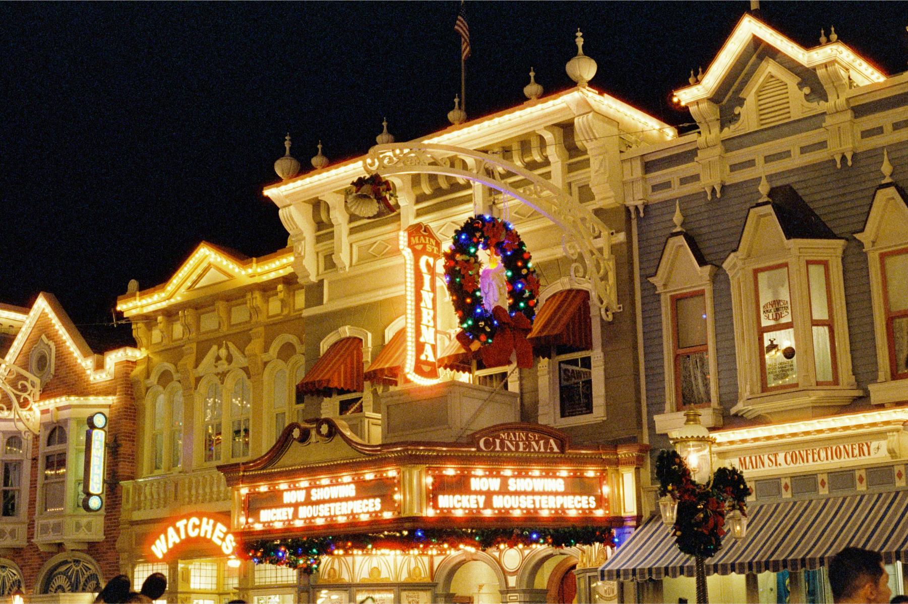 Main Street Cinema at Magic Kingdom decorated with Christmas lights and holiday wreaths at night.